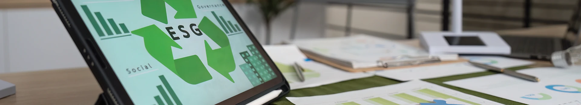 Tablette affichant une analyse ESG avec graphiques de durabilité dans un bureau moderne, entourée de documents et d’éléments visuels sur la gouvernance, l’environnement et le social.