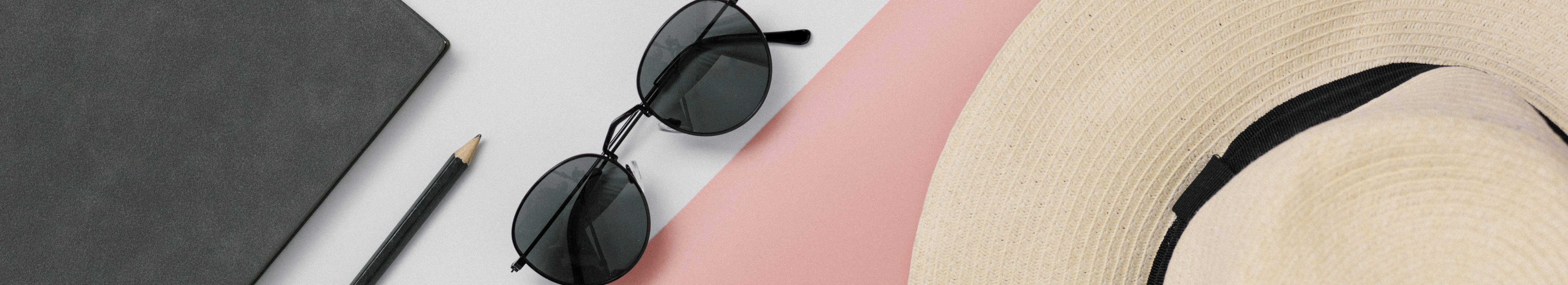 Carnet fermé, lunettes de soleil et chapeau posés sur une table claire, suggérant une pause estivale tout en gardant un œil sur la trésorerie.